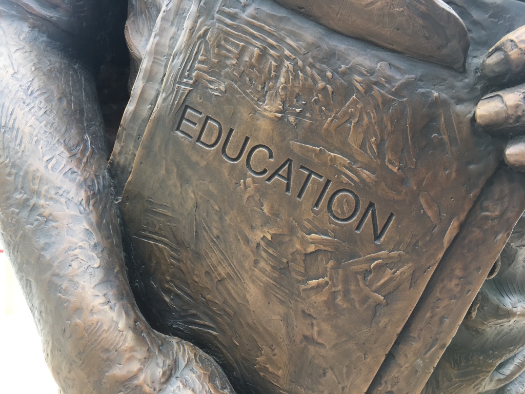 Photo has a closeup of the part of a statue where it has a sign that says "Education."
