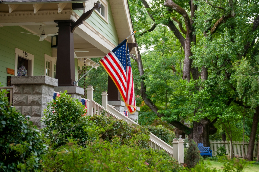 Photo is of an American flag hanging in front of a house.