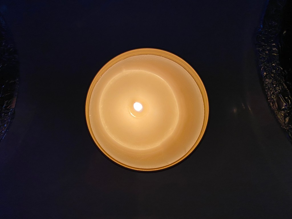 Photo is the top view of a lit white candle with a black background.